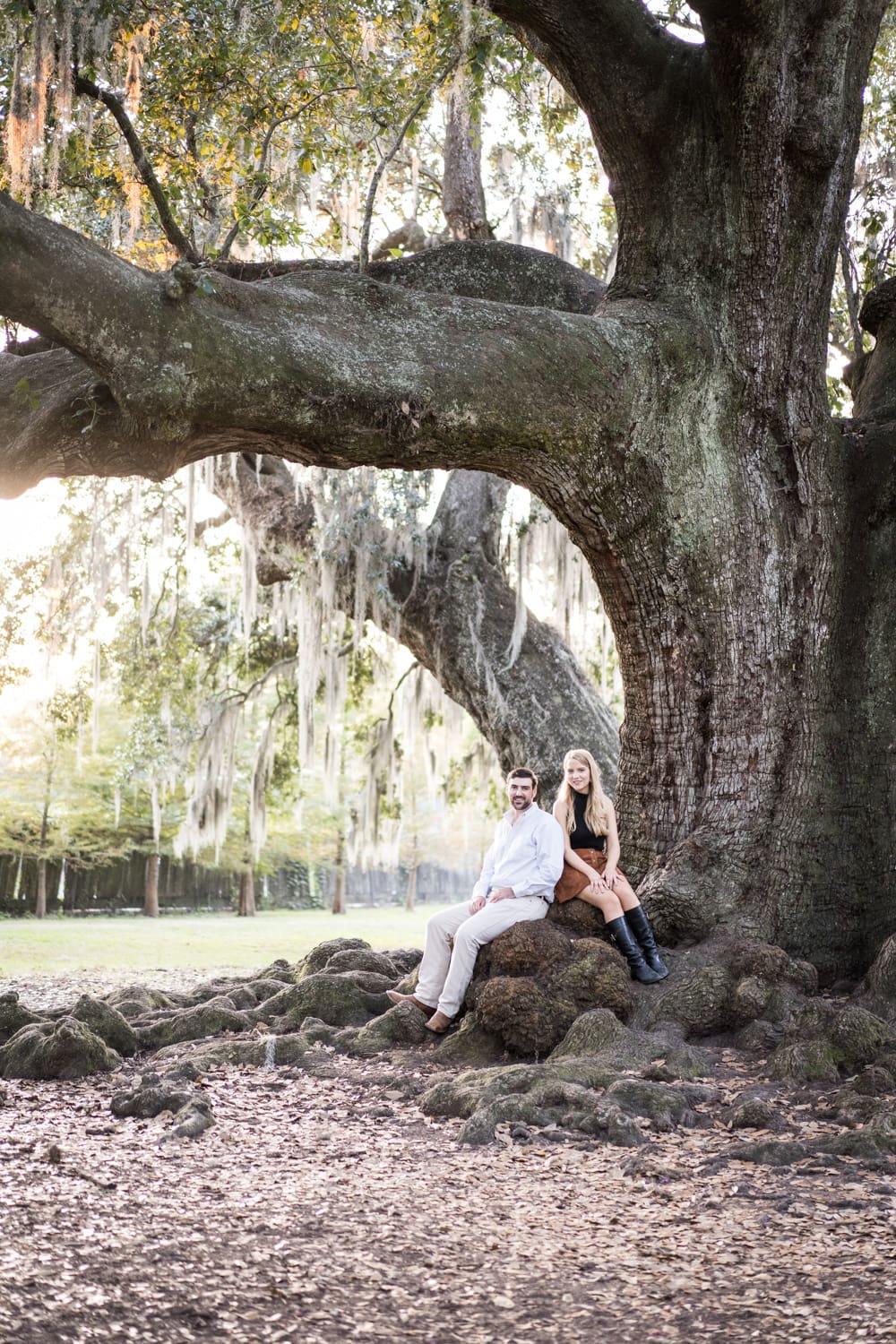 Couple sitting by large oak tree during engagement portrait session in Audubon Park