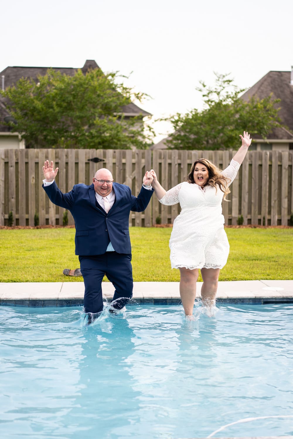 Bride and groom jumping into backyard pool