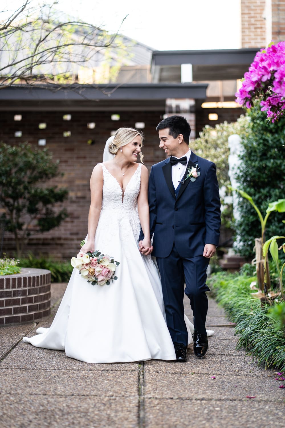 Bride and groom walking in garden area next to church