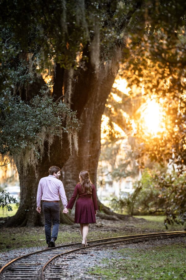 Couple walking along railroad tracks with sun in background