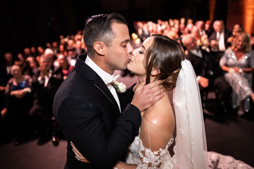 Bride and groom kiss at Civic Theatre wedding with guests in the background