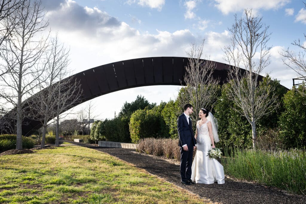 Bride and groom with Rusty Rainbow Bridge in background in Crescent Park