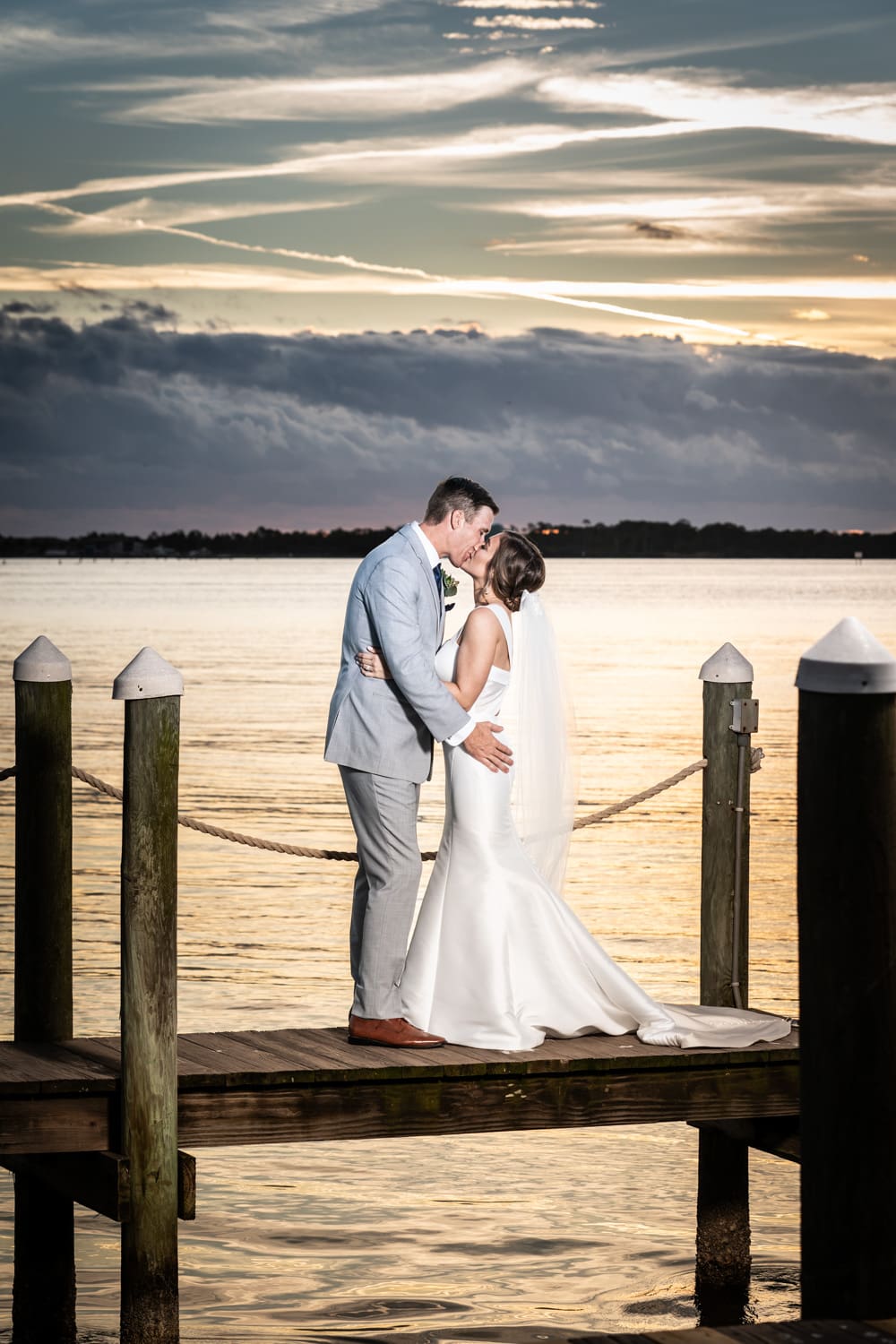 Beach wedding portrait of bride and groom on dock with dramatic sunset