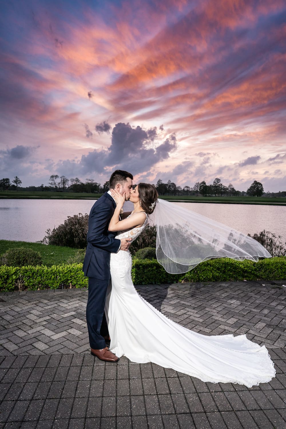 Bride and groom kissing with dramatic sunset behind them at English Turn Country Club wedding