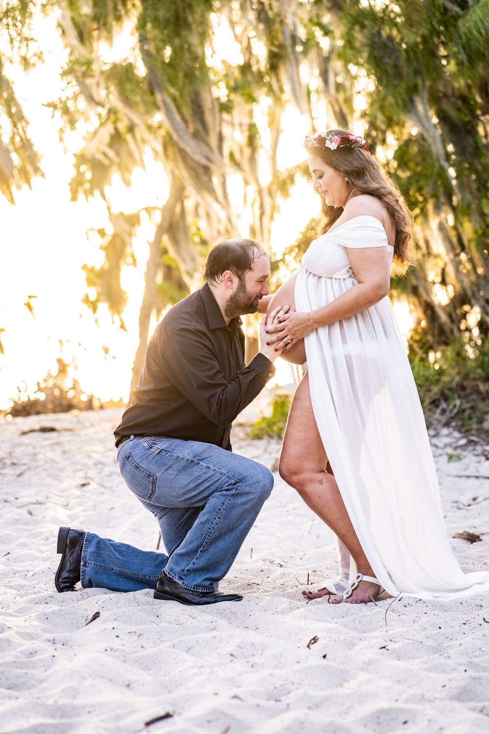 Maternity portrait of husband kissing wife's tummy with brilliant sunlight in background