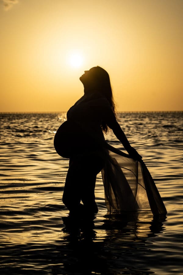 Maternity portrait of pregnant mother in the water silhouetted against sunset