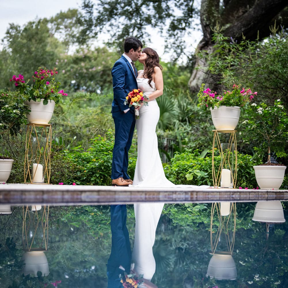 Couple kissing with reflection in pool at New Orleans backyard wedding