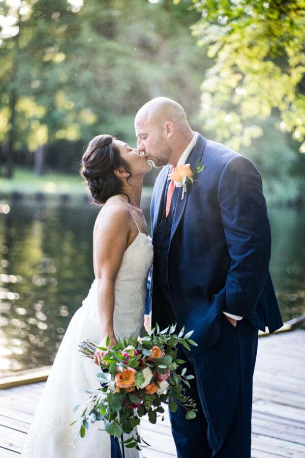 Bride and groom kiss on dock by water