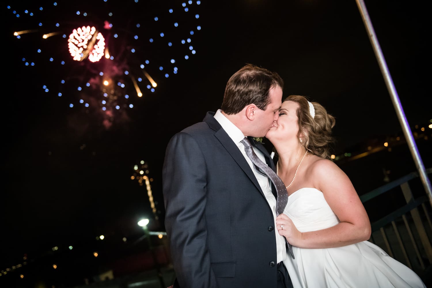 Bride and groom kiss at Pat O's on the River with fireworks in the background