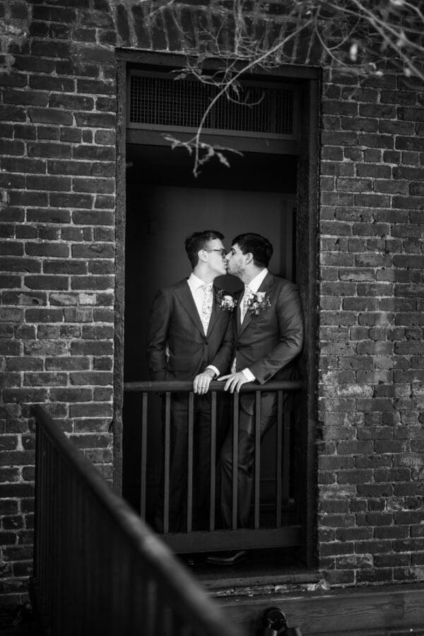 Grooms kissing in window opening on balcony