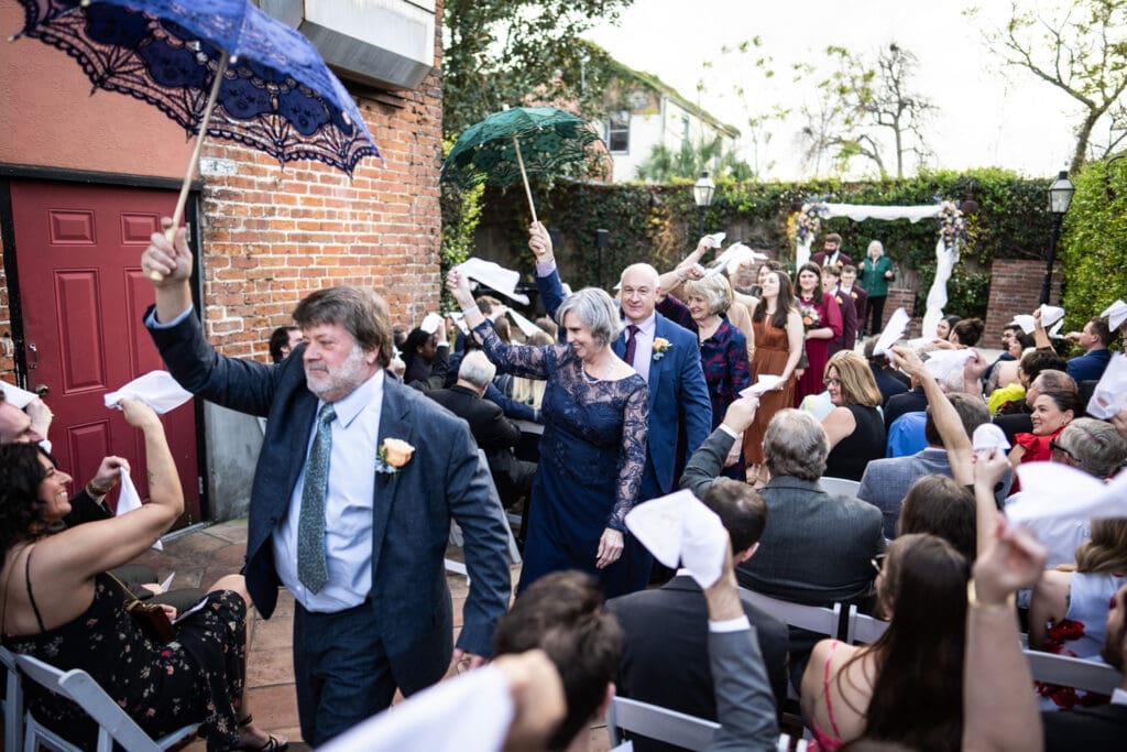 Parents and guests second line parade down the aisle with umbrellas