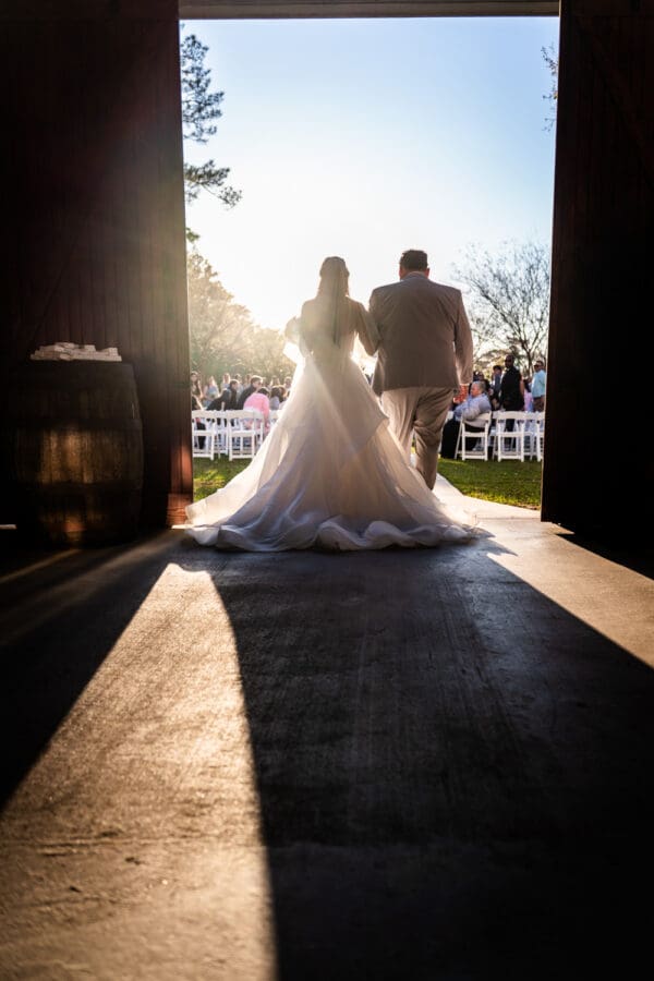 Backlit view of bride and father walking through doorway at beginning of wedding ceremony