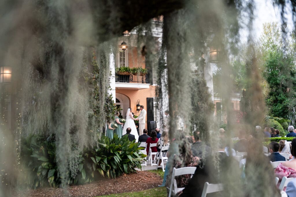 Looking through mossy oak tree at bride and groom on porch at Southern Oaks