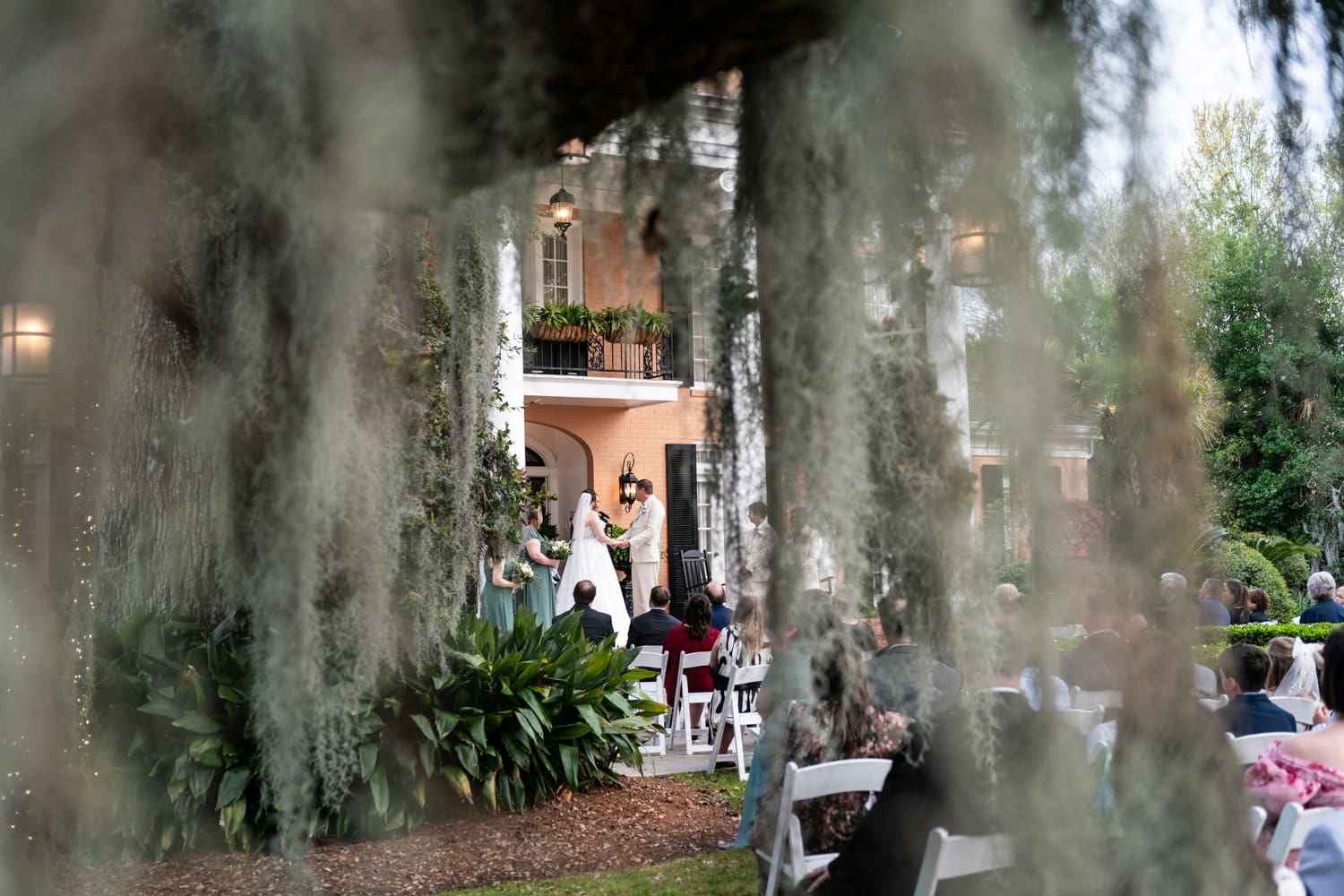 Looking through mossy oak tree at bride and groom on porch at Southern Oaks