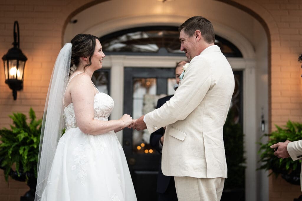 Bride and groom hold hands on porch of Southern Oaks during wedding ceremony