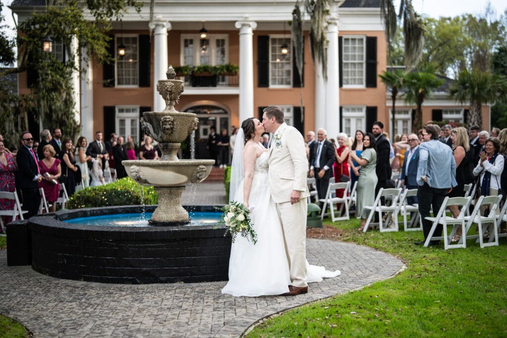 Bride and groom kiss on walkway by fountain at Southern Oaks