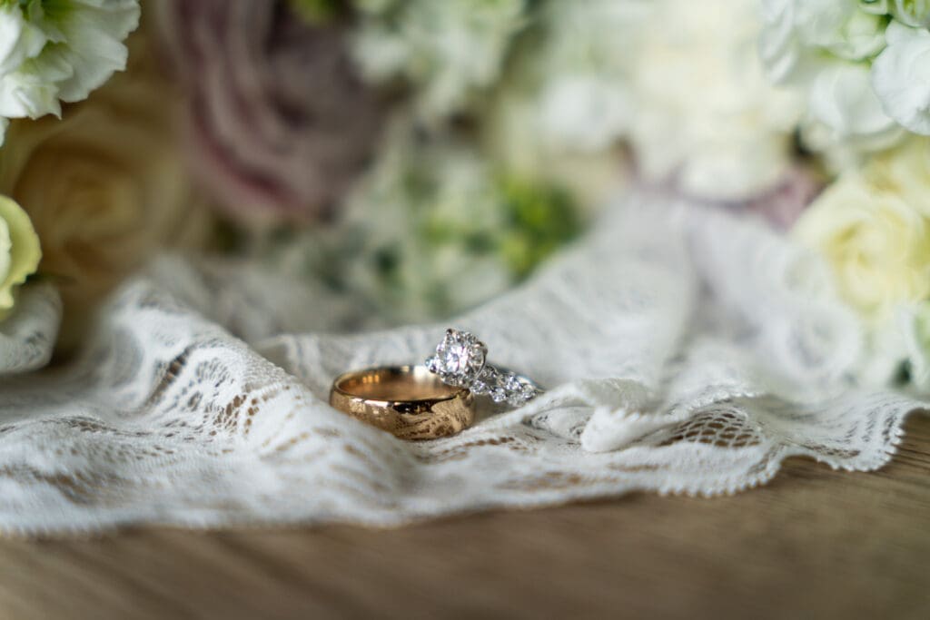 Wedding rings on lace cloth with flowers in the background