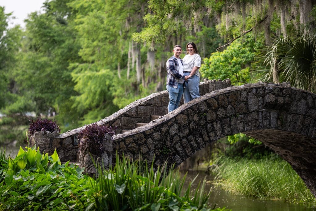 Couple holding hands as they stand on stone bridge in park