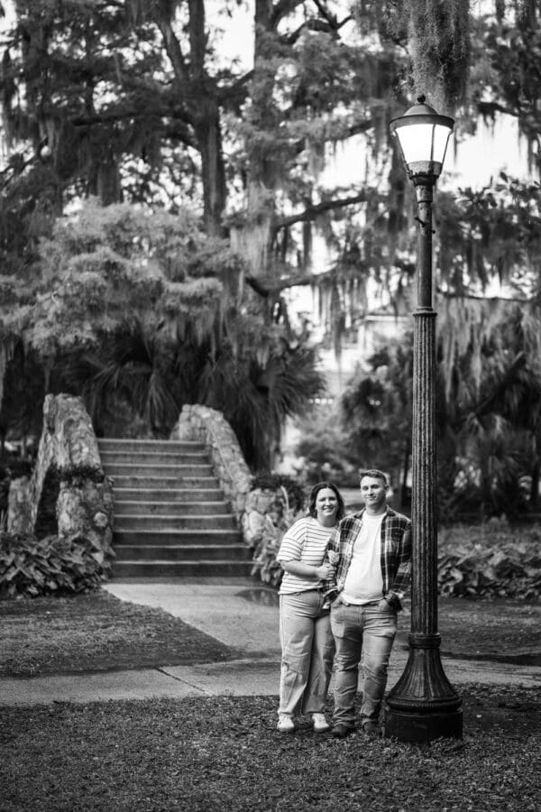 Couple leaning up against lamp post with stone bridge in the background