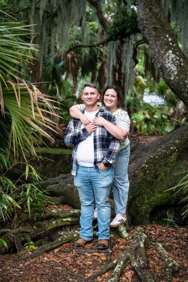Couple embracing as they stand in front of moss-covered tree
