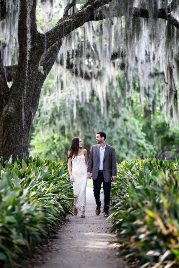 Couple walks along pathway in park with moss covered trees behind them