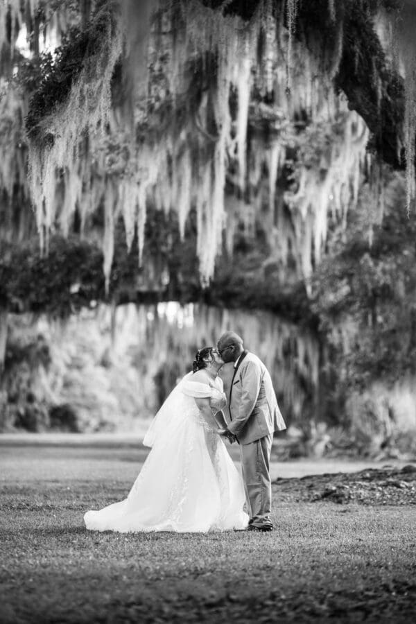 Bride and groom kissing under moss-covered oak trees at Fontainebleau State Park