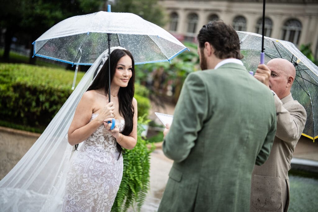 Bride smiling at groom while holding an umbrella in the rain