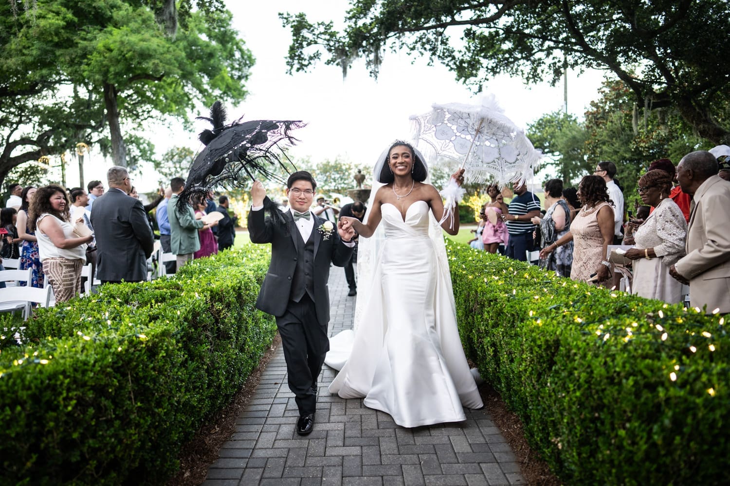 Bride and groom celebrate as they walk up the aisle at Southern Oaks holding umbrellas