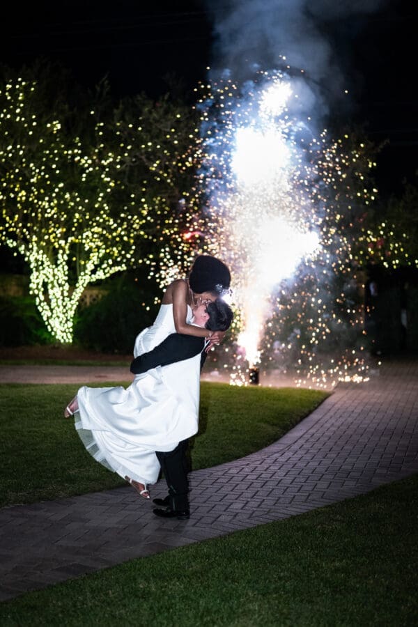 Groom lifts and kisses bride with fireworks in the background