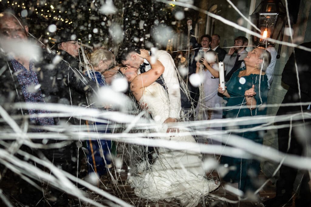 Bride and groom kiss amongst confetti and streamers