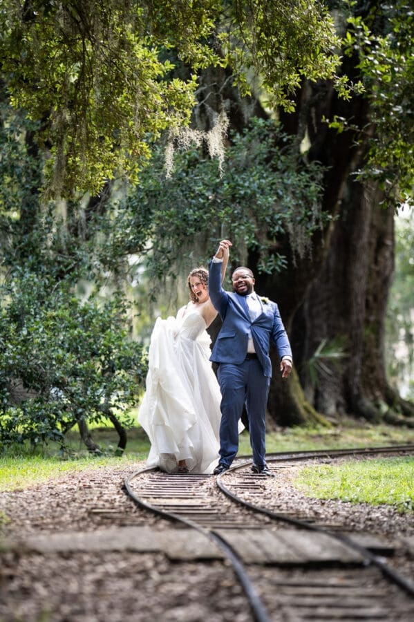Bride and groom celebrate as they walk along railroad tracks in City Park