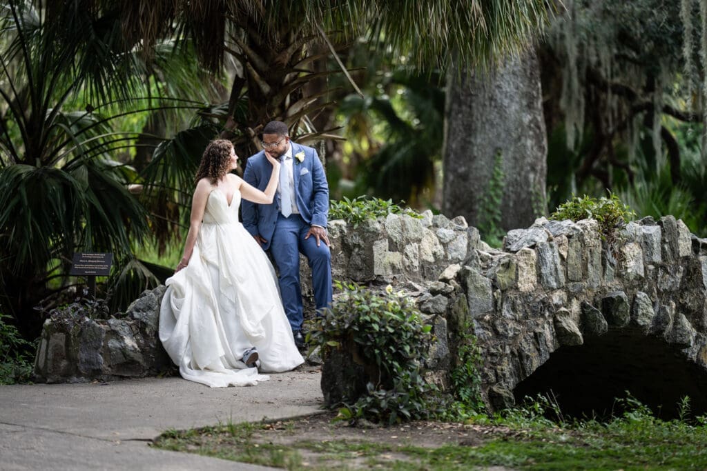 Bride touches groom's face while sitting on stone bridge in City Park
