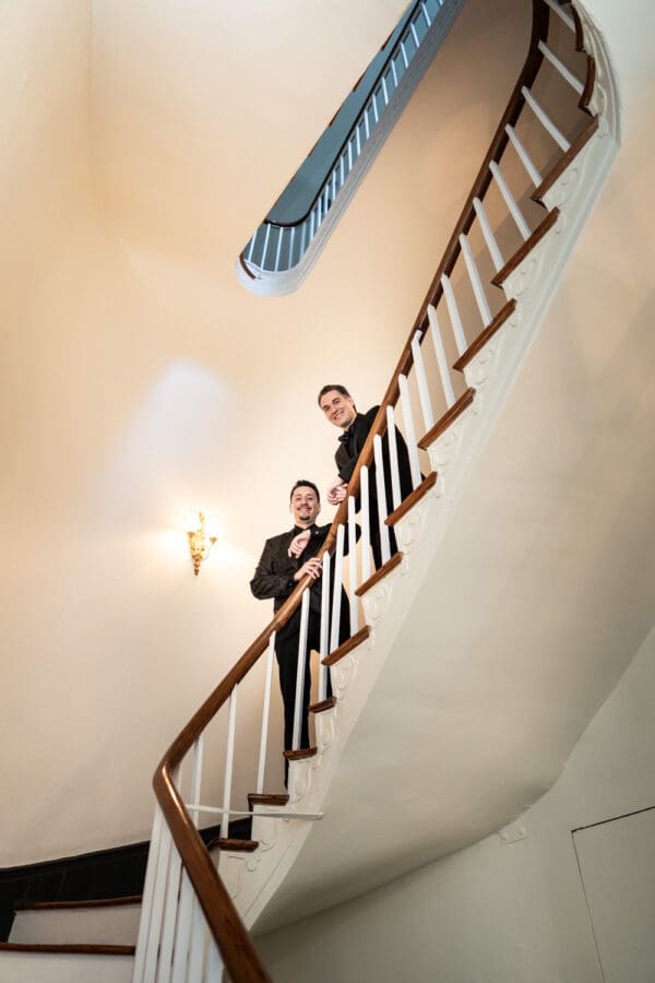 Two grooms looking over railing of spiral staircase