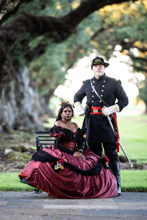 Man and woman in Civil War era attire by wrought iron bench at Oak Alley