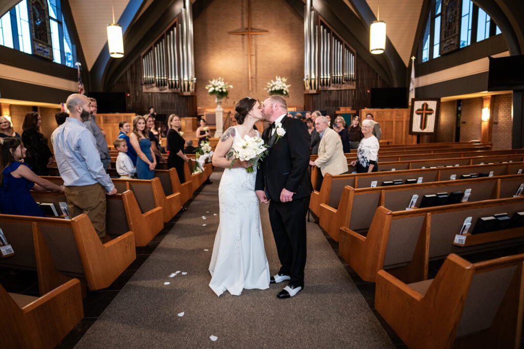 Bride and groom kiss in the church aisle